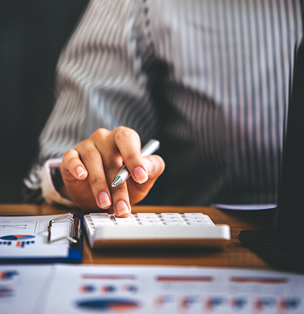 Accountant using a calculator over printed financial statements and charts while preparing a contractor's financials