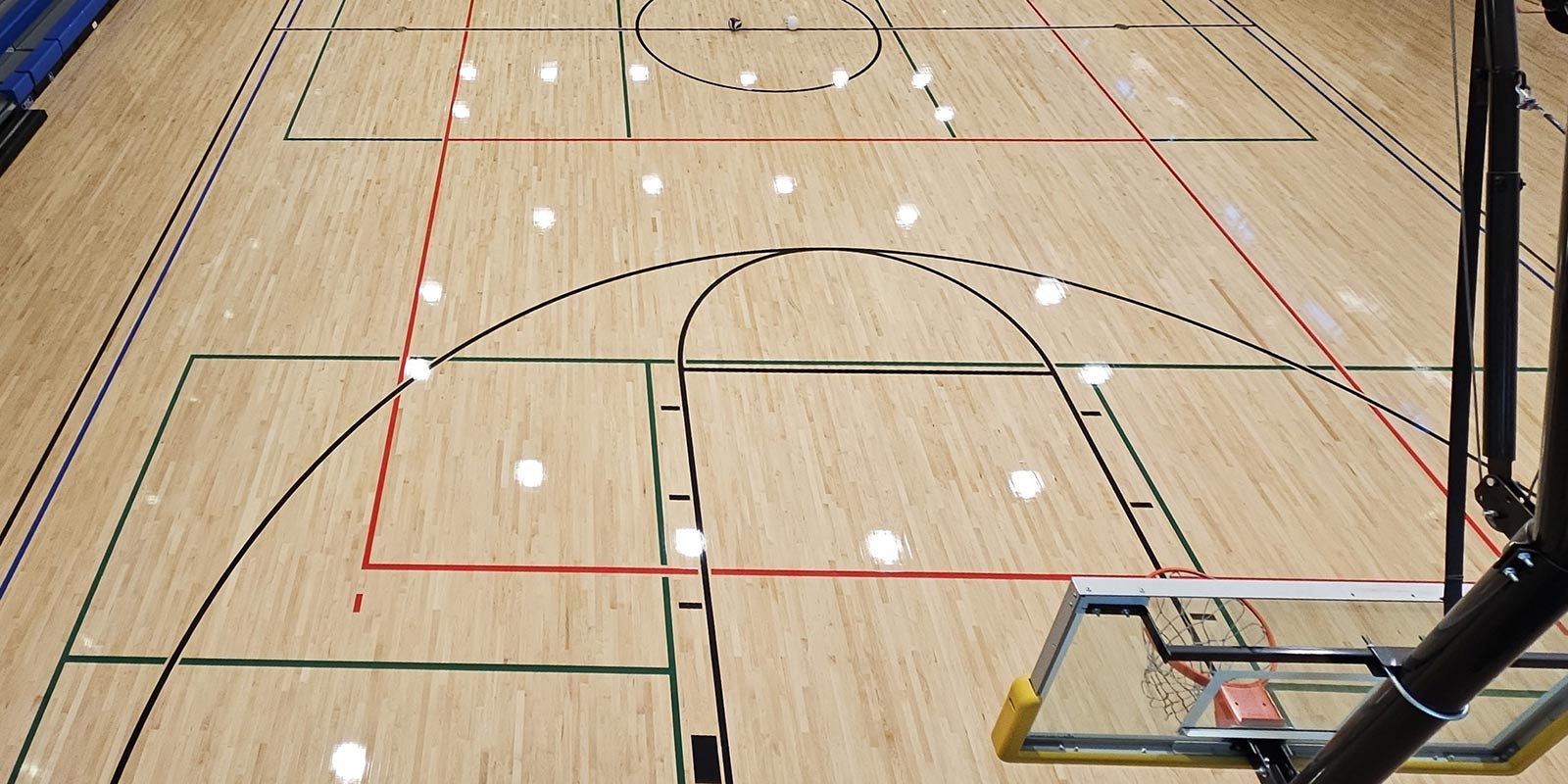 Newly finished hardwood gymnasium floor with basketball backboard and painted court lines