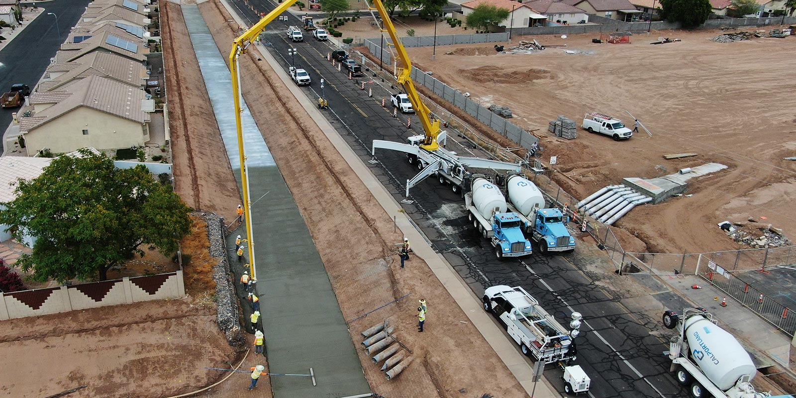 Concrete pump truck and mixers placing a lined drainage channel along a residential street